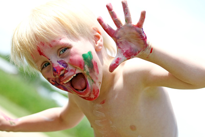 A happy young preschool aged child is smiling at the camera while his face is covered in messy paint